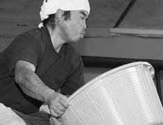 蒸し上がった米を担ぎ、タンクへ運ぶ